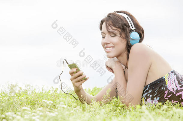 <strong>年</strong>轻女子躺在草地上对着晴朗的天空用耳机听音乐的侧视图