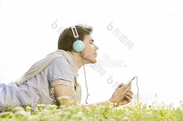 在<strong>晴朗</strong>的天空下，在公园里用耳机欣赏mp3音乐的人的侧视图