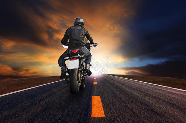 年轻人骑着大摩托车在柏油路上迎着美丽的昏暗天空