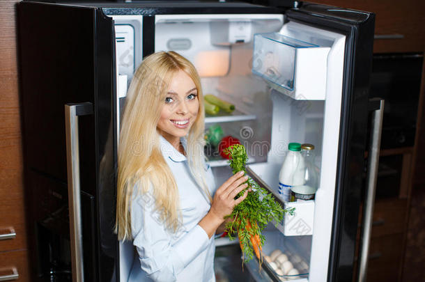 一个年轻的女人在冰箱旁边拿着健康的食物。