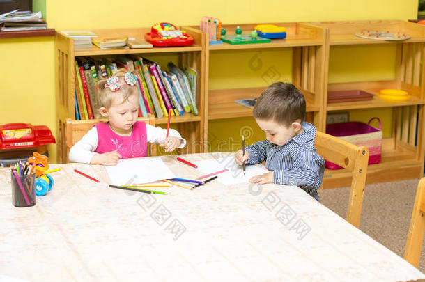 两个小朋友在桌边用彩色铅笔画画。幼儿园男女生画画