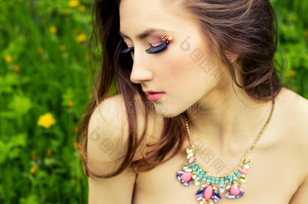 美丽的年轻女孩，长发，美丽的妆容，脖子上戴着项链，坐在花园里的草地上