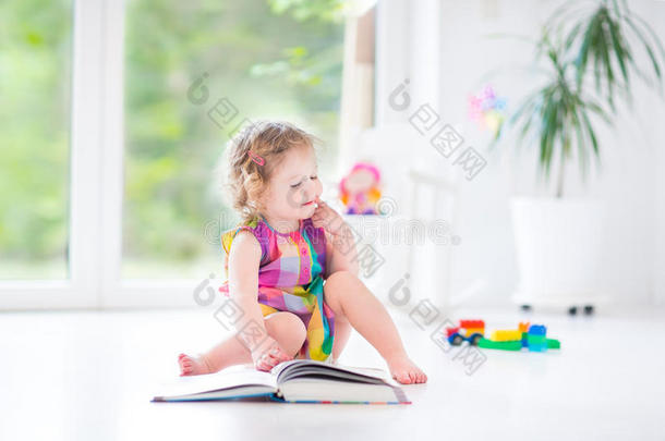 有趣的幼儿女孩在阳光明媚的卧室里看书