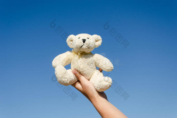 蓝色天空背景下，手上拿着毛茸茸的泰迪熊