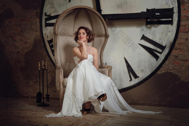 穿着婚纱，坐在奇怪的<strong>椅子</strong>上微笑的女孩。新娘坐在<strong>椅子</strong>上，背景是钟表和壁炉用具。