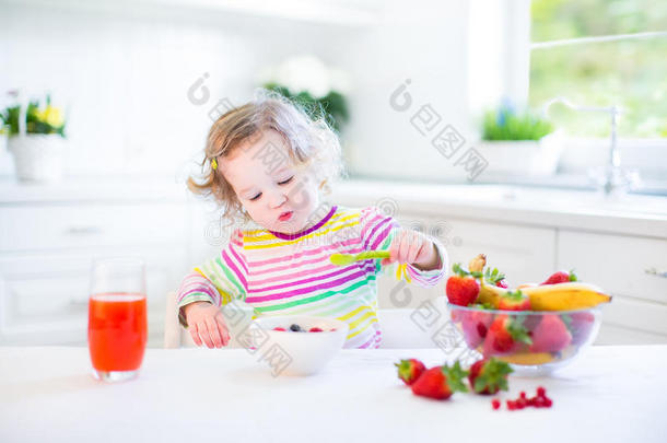 可爱的蹒跚学步的女孩吃早餐喝果汁