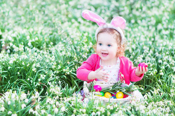 带着兔子耳朵的蹒跚学步的女孩和春天花朵里的蛋