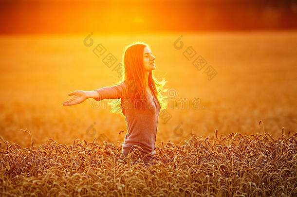 在麦田里高举双臂享受阳光的年轻女子