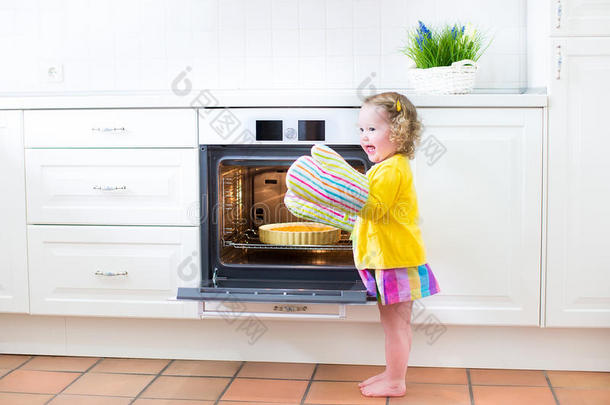 厨房里的小女孩戴着连指手套，旁边放着苹果派