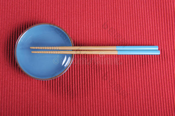 水蓝色的筷子和碗放在红色的垫子桌上。