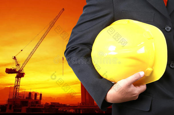 工程师手持黄色头盔为工人安全背景的新高层建筑和剪影起重机升降机