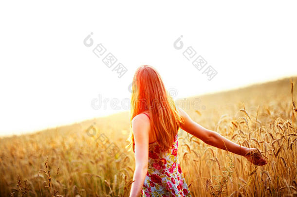 在麦田里高举双臂享受阳光的年轻女子