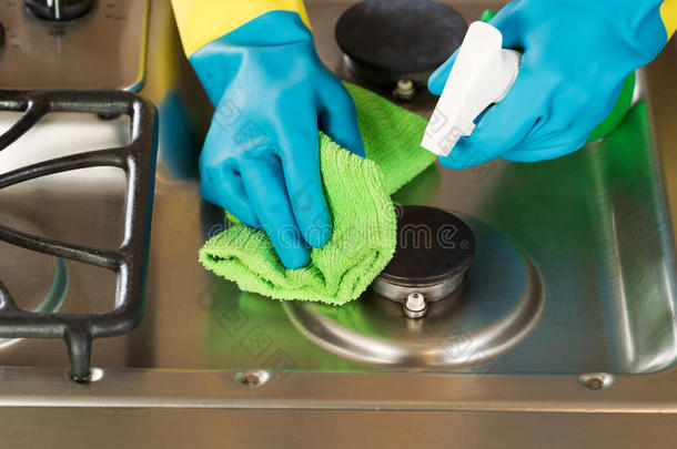戴手套的手清洁炉灶顶部，带有喷雾瓶和超细纤维抹布