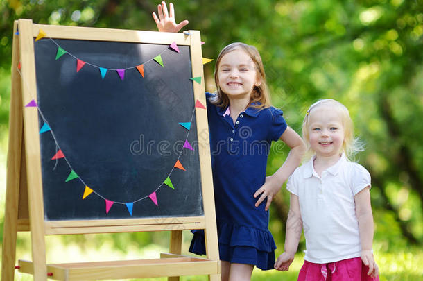 两个兴奋的小姐妹坐在黑板旁
