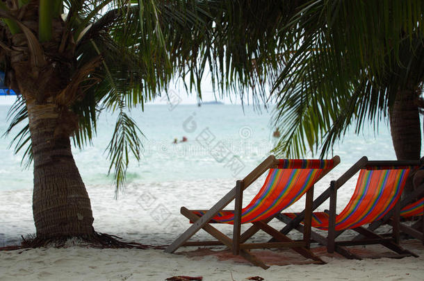 海边棕榈树下的沙滩上的两张沙滩椅