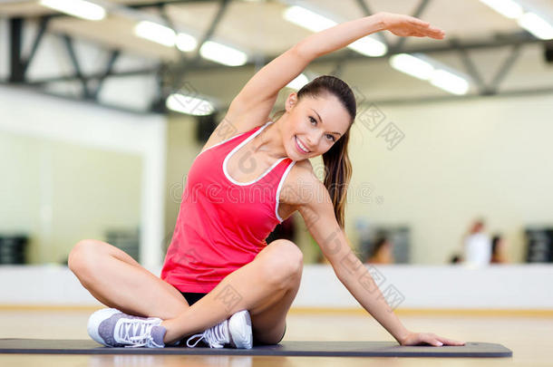 微笑的女人在健身房的<strong>垫子</strong>上伸展