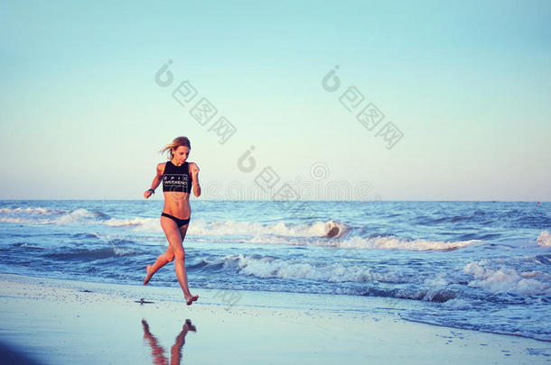 迷人的女跑步者在迷人的日落下沿着海滩奔跑，背景是大海