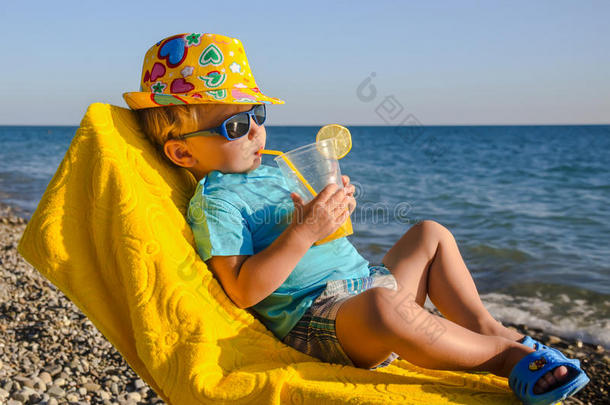 沙滩上坐在扶手椅上拿着果汁杯的男孩