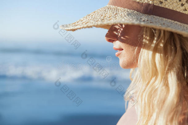 美丽的金发女郎戴着草帽在沙滩上微笑