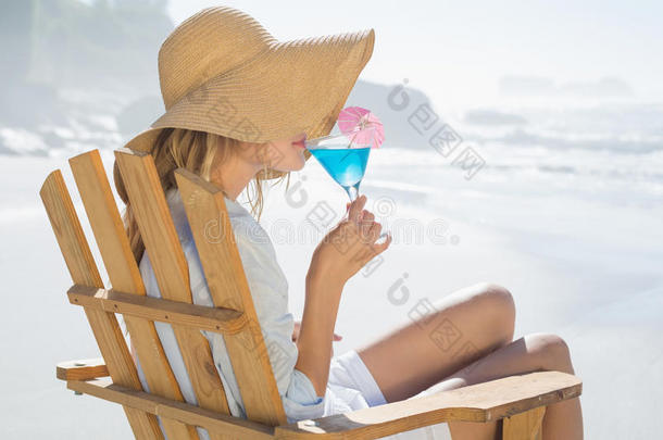 笑容可掬的金发女郎在海边的躺椅上休息，啜饮着鸡尾酒