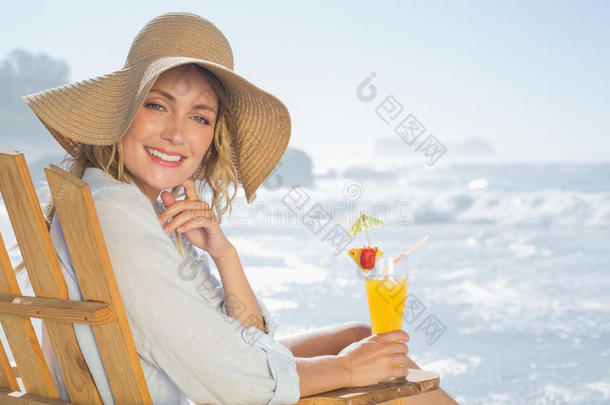 笑容可掬的金发女郎在海边的躺椅上休息，手里拿着鸡尾酒