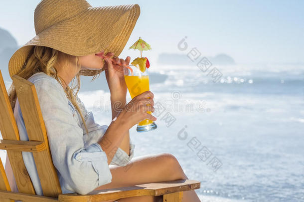 笑容可掬的金发女郎在海边的躺椅上休息，啜饮着鸡尾酒