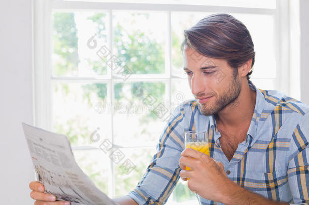 漫不经心的微笑的男人一边看报纸一边喝着橙汁