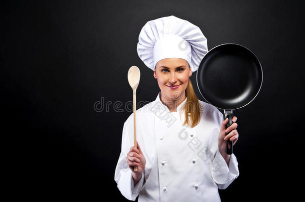 黑暗背景下年轻的女厨师用不同的工具