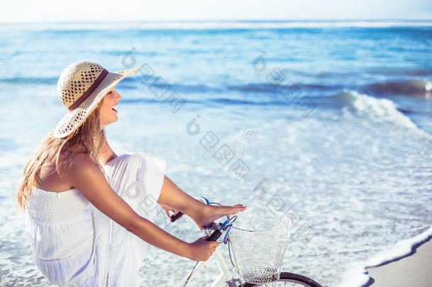 美丽的金发女郎穿着白色太阳裙在沙滩上骑自行车