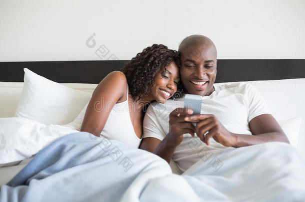 一对幸福的情侣抱着智能手机躺在床上