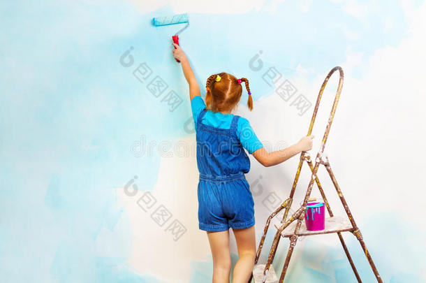 穿蓝色衣服的小女孩在梯子上油漆墙壁