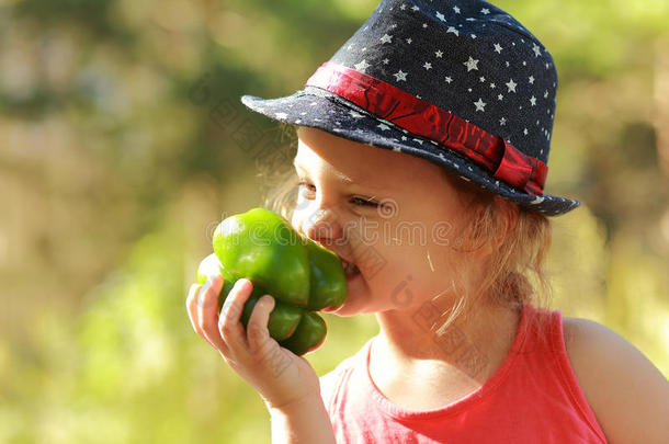 有趣的小女孩戴帽子吃大青椒