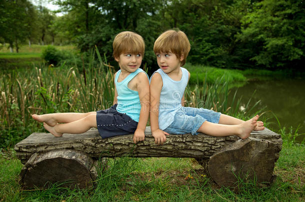 可爱的<strong>双胞胎兄弟</strong>坐在木凳上，微笑着看着美丽的湖边的对方