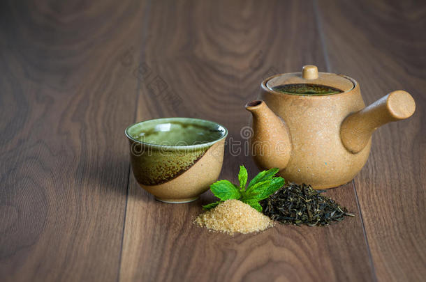 陶瓷茶壶，一杯红茶，薄荷叶和红糖放在木桌上。