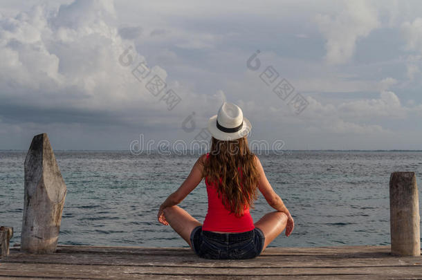 年轻女子盘腿坐在海边欣赏日落