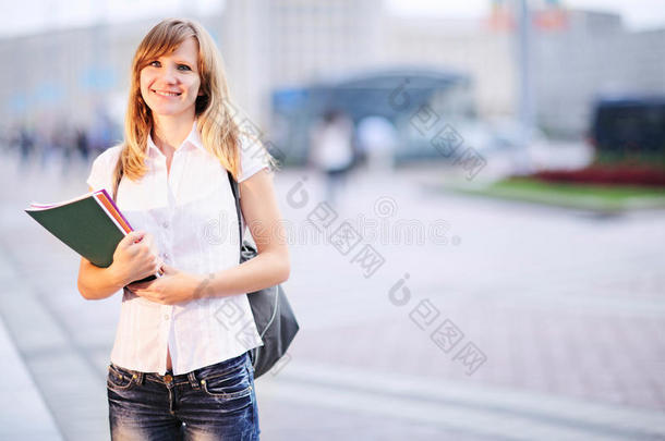 年轻的学生，美丽的白种女人，早上站在模糊的大学建筑背景上。