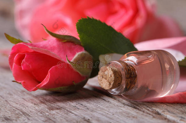 玻璃瓶中的玫瑰油和木制桌子上的粉色花朵