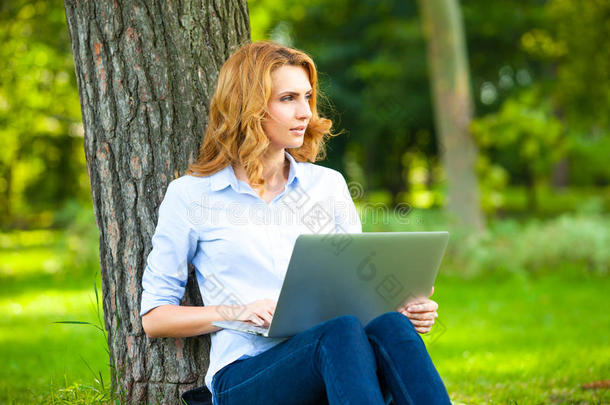 <strong>坐在公园里</strong>的漂亮女人拿着笔记本电脑