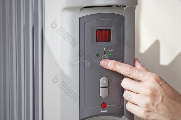一个女人的手在一个数字可编程油加热器上设定室温