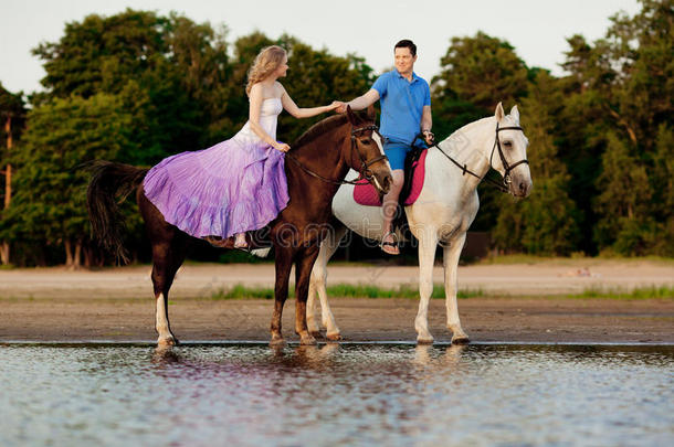两个<strong>骑</strong>马的人在海滩上日落时<strong>骑</strong>马。情侣<strong>骑</strong>马。年轻漂亮的男人和女人在海上<strong>骑</strong>马。
