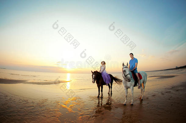 两个<strong>骑</strong>马的人在海滩上日落时<strong>骑</strong>马。情侣<strong>骑</strong>马。年轻漂亮的男人和女人在海上<strong>骑</strong>马。