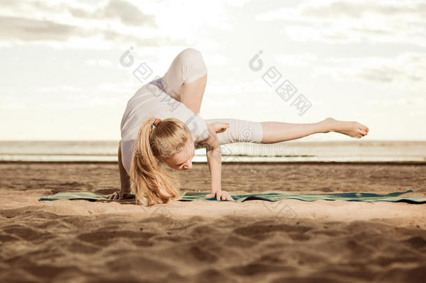 夕阳下，美丽苗条的年轻女子在海滩上练习瑜伽