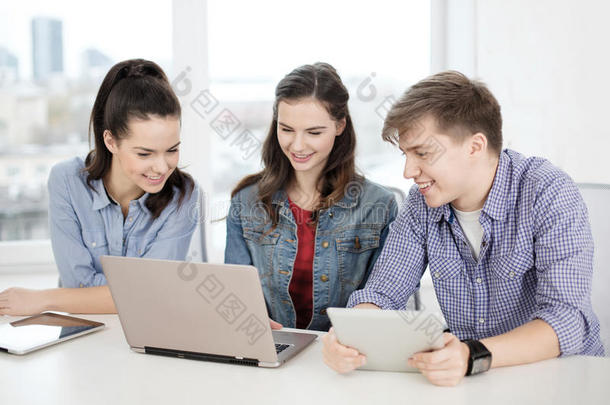 三个面带微笑的学生拿着笔记本电脑和平板电脑