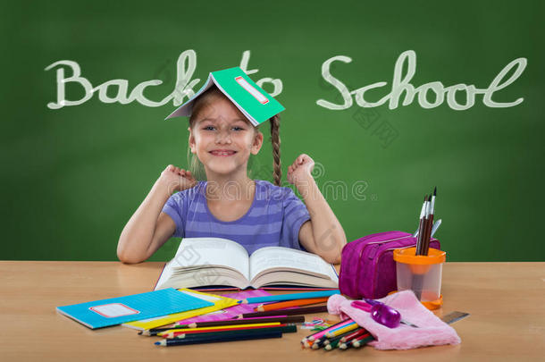 快乐的小女孩坐在学校的长椅上，后面黑板上有返校的牌子