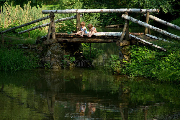 可爱的<strong>双胞胎兄弟</strong>坐在木桥边，在美丽的湖边钓鱼