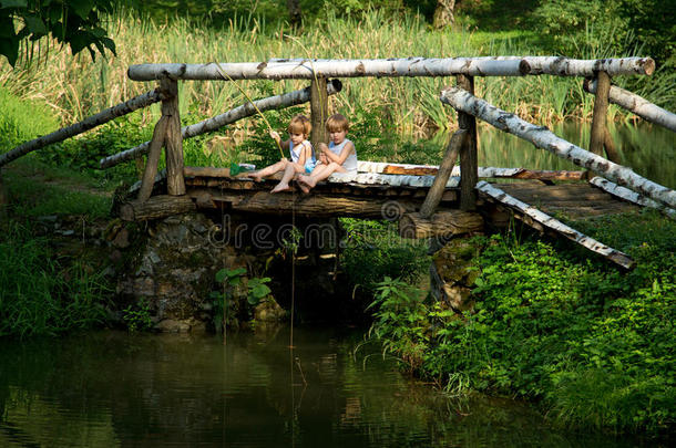 可爱的双胞胎兄弟坐在木桥边，在美丽的湖边钓鱼