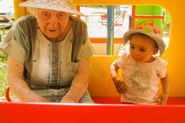 年纪很大的奶奶和她的小孙女在操场上聊天，都戴着帽子，红色的白板