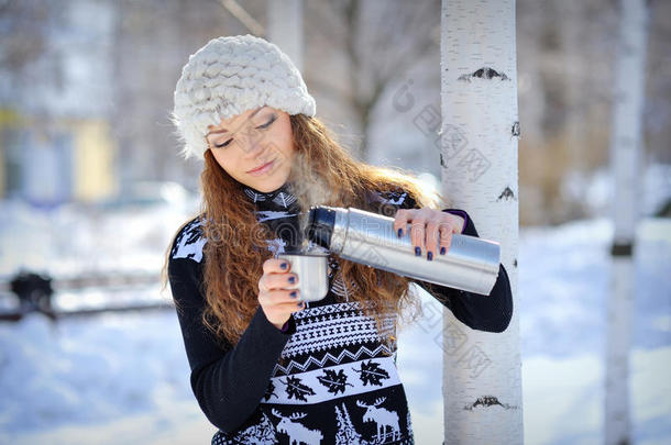 在寒冷的冬日里，美丽的女孩拿着保温瓶和杯热茶