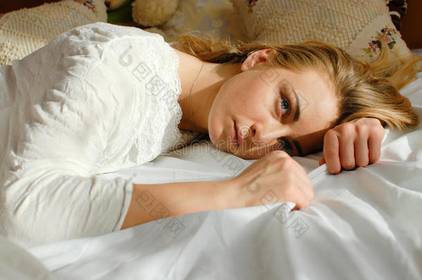 情感美丽的金发年轻女士放松躺在床上看着卧室背景特写空间的肖像