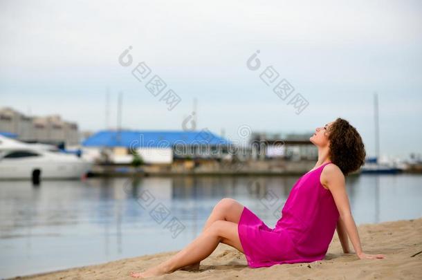 一个穿着<strong>红色</strong>连衣裙卷发的年轻女子坐在<strong>海边</strong>